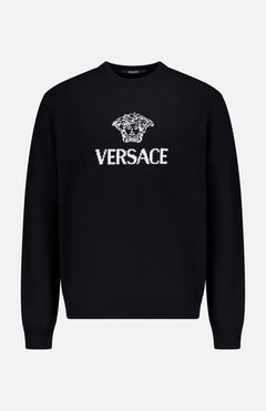 The Medusa Cashmere Knit Sweater by VERSACE is a black crewneck with long sleeves, showcasing the iconic Medusa logo and bold white VERSACE branding on the front—a standout in luxury Italian menswear.