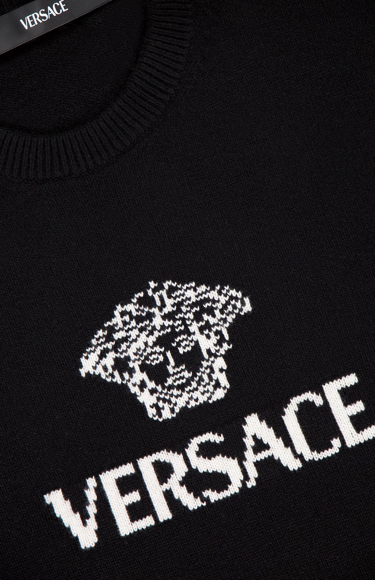 Close-up of the black VERSACE Medusa Cashmere Knit Sweater, showcasing the white Medusa logo and VERSACE text knitted on the front; brand label visible inside the collar.