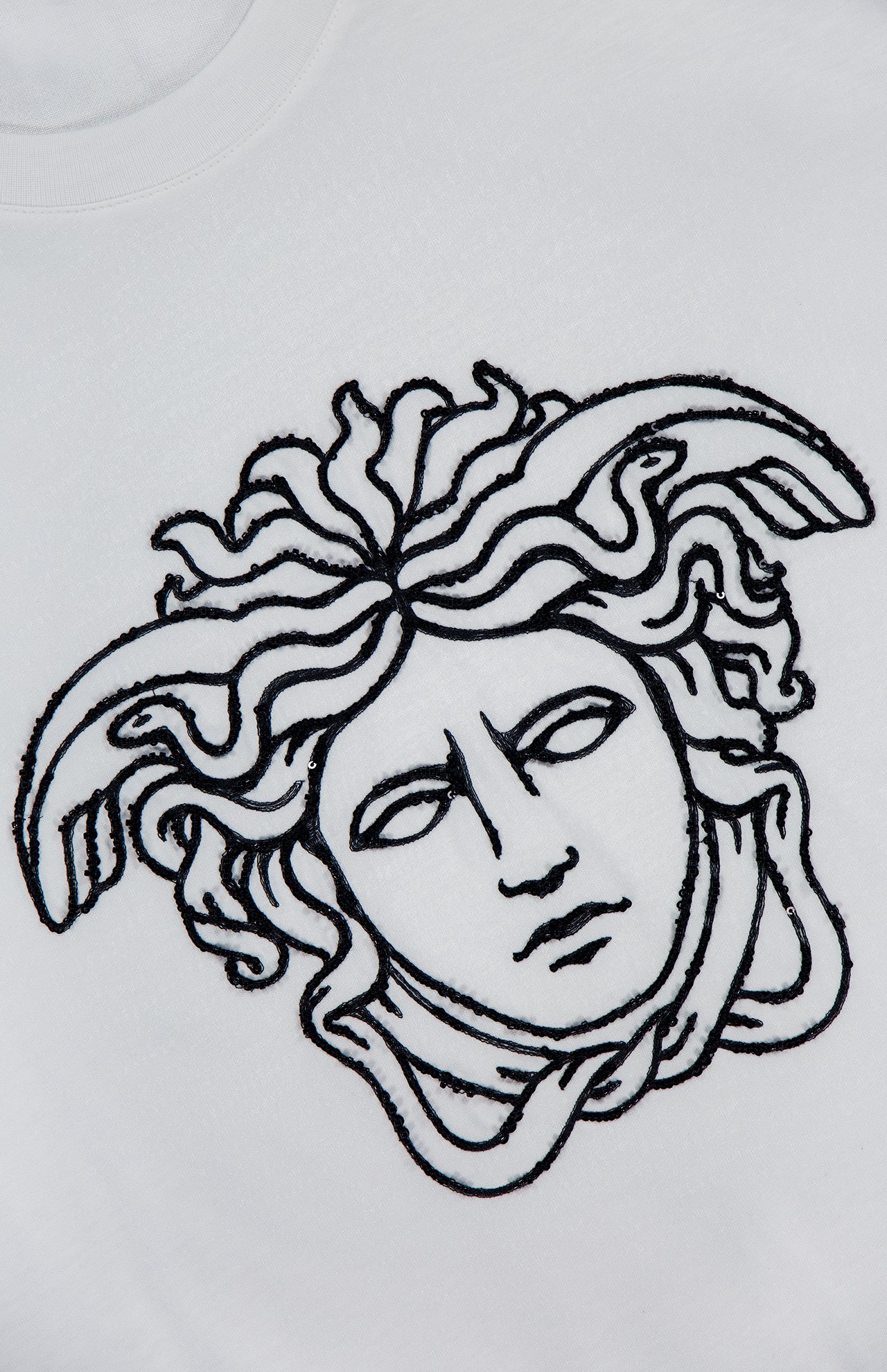 The VERSACE Cotton Jersey Medusa Embroidery T-Shirt features a black embroidered outline of the mythological Medusa head with snake hair on white fabric, capturing the essence of luxury Italian fashion.