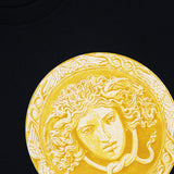 The Cotton Medusa Coin Jersey T-Shirt by VERSACE epitomizes luxury Italian men’s fashion with its bold central Medusa coin graphic, encircled by an ornate border. Featuring the iconic Versace logo in elegant gold lettering at the hem, this black t-shirt makes a striking addition to any contemporary wardrobe.