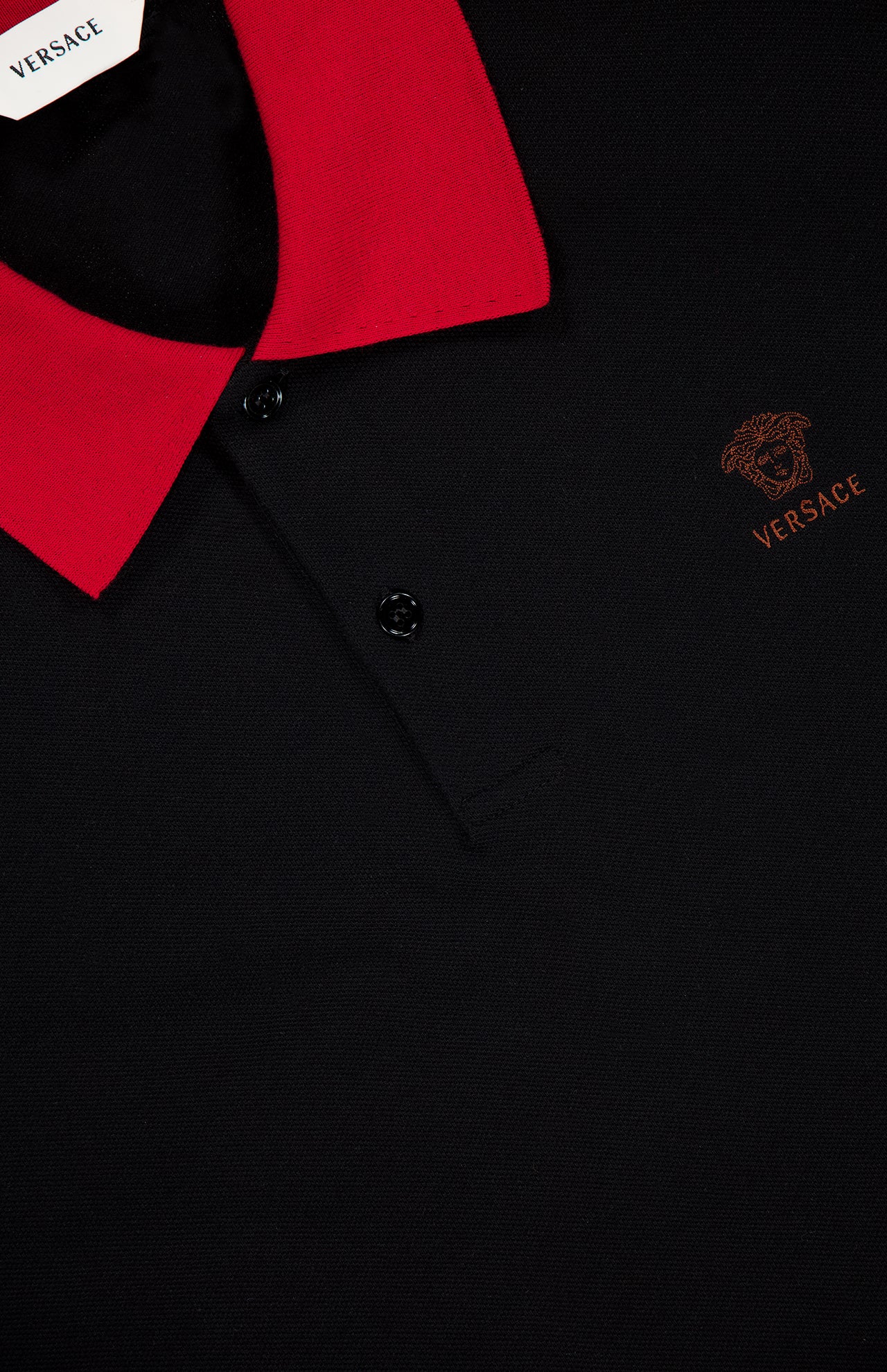 Close-up of the VERSACE Medusa Logo Embroidery Piquet Polo Shirt, showcasing its red collar, black buttons, and brown embroidered Medusa logo on the chest.