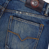 Close-up of VERSACE Non-Stretch Dirty Wash Jeans in Dirty Blue, showing a back pocket with yellow stitching and a black leather Medusa logo label above the waistband.