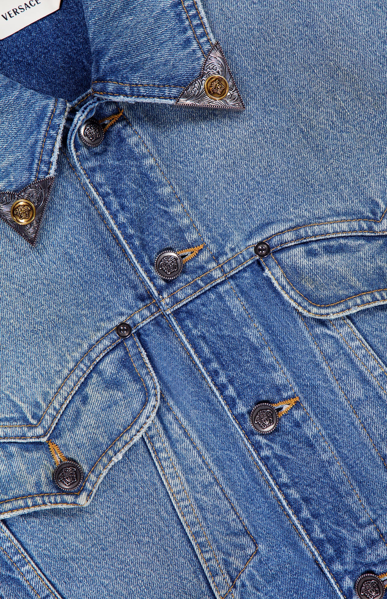 Close-up of the VERSACE Rigid Stone Washed Denim Jacket highlights its bold stitching, signature Medusa logo buttons, and a peek at the white collar label—exemplifying high-end Italian craftsmanship.