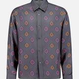 The VERSACE Silk Twill Print The Suitor Shirt is a luxury Italian menswear piece featuring long sleeves, a button-up front, dark gray base, orange, purple and pink geometric print, collar, and visible green edge stitching.