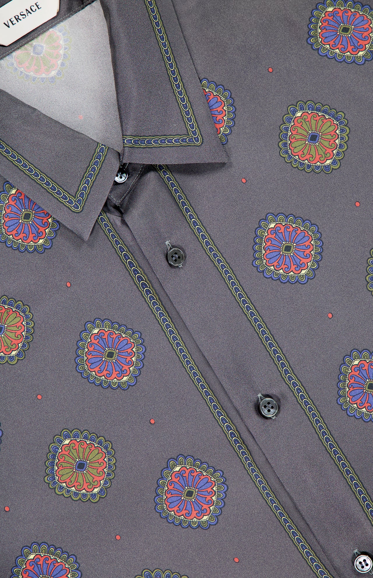 Close-up of the VERSACE Silk Twill Print The Suitor Shirt in gray silk, showcasing its vibrant red, blue, yellow, and green print with black buttons and detailed stitching along the collar and placket.