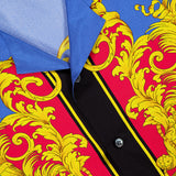 Close-up of VERSACE's Silk Twill Print The Sun Shirt, a luxury Italian menswear piece in blue and red silk with ornate yellow baroque print, black vertical stripes, sun motifs, black buttons, and a visible collar.