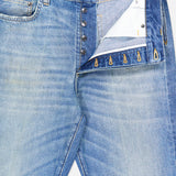 A close-up of the VERSACE Stone Washed Rigid Jeans with the fly open, featuring metallic buttons, a white inner lining, and a visible VERSACE label on the inner waistband.