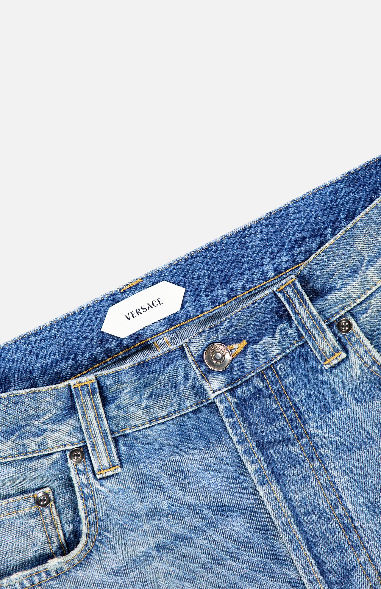Close-up of light blue VERSACE Stone Washed Rigid Jeans, highlighting the waistband, front button, belt loops, and a glimpse of the signature brand label—an essential detail for those looking for men’s designer jeans in a classic straight-leg fit.