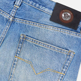 Close-up of light blue VERSACE Stone Washed Rigid Jeans featuring a back pocket with yellow stitching and a black leather VERSACE label with the Medusa logo on the waistband—an iconic detail of these men’s designer straight-leg jeans.