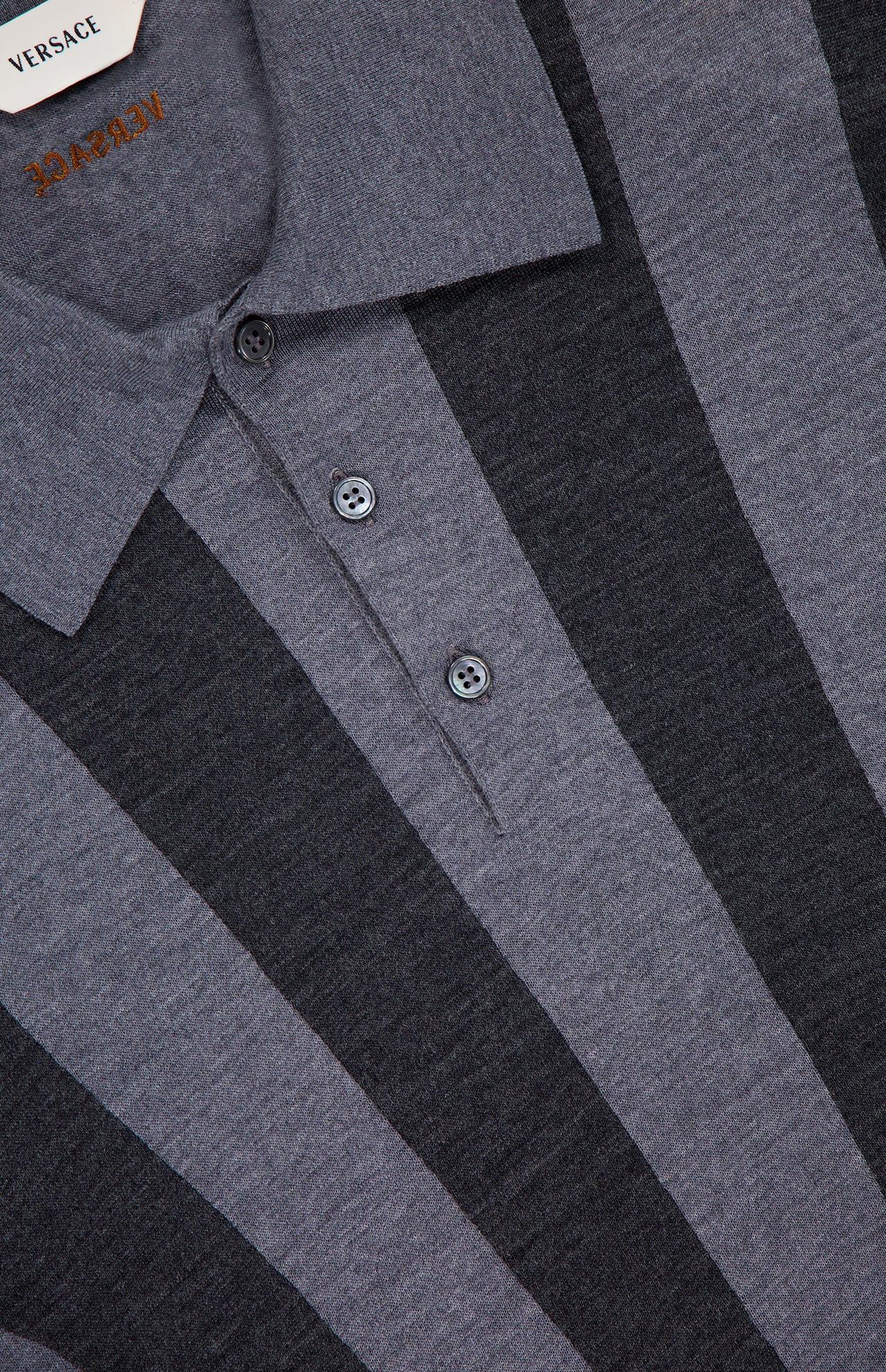 Close-up of a luxury VERSACE Sweater Rays Intarsia Knit Polo, featuring vertical dark and light gray stripes, a two-button placket, visible collar, and the partially shown Versace label at the top left.