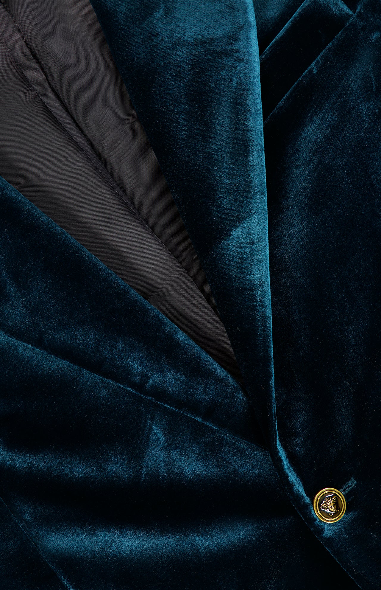 Close-up of the VERSACE Viscose Silk Liquid Velvet Evening Jacket for men in dark green, showcasing a gold decorative button that accentuates the luxurious liquid velvet texture, with a hint of the sleek black inner lining—evoking the refined elegance characteristic of Versace eveningwear.
