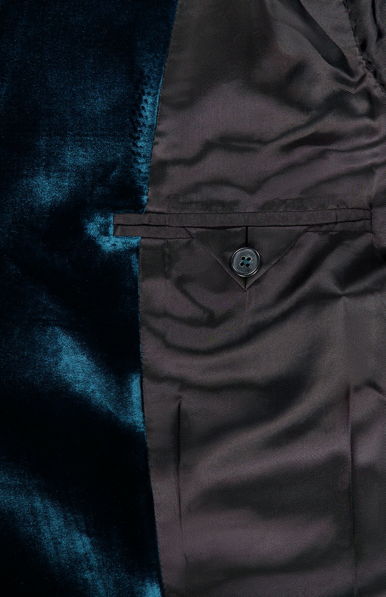 Close-up of the VERSACE Viscose Silk Liquid Velvet Evening Jacket’s inner lining, highlighting its lustrous dark brown fabric, buttoned interior pocket, and rich deep blue velvet detail on the left side—an exquisite feature that enhances this men’s luxury blazer.