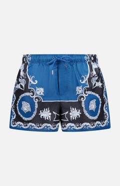 VERSACE Mythic Barocco Print Swim Shorts: blue and black with a white ornate floral and scroll baroque motif, featuring a drawstring waistband and mid-thigh length. Luxury Italian swimwear style.