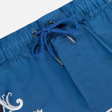 Close-up of VERSACE Mythic Barocco Print Swim Shorts in blue, featuring a white floral motif, silver eyelets, and fine stitching details that highlight the sophisticated Italian-inspired design.