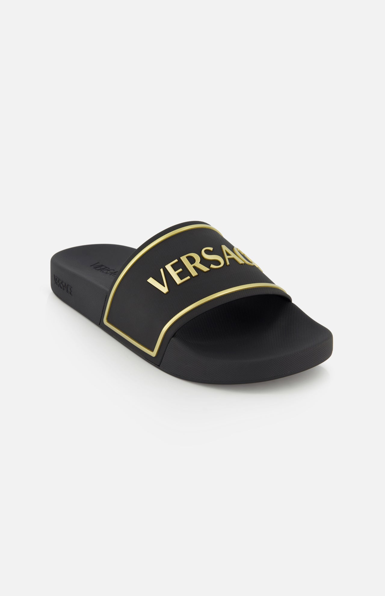 The Rubber + Embossing Versace Slide Sandals by VERSACE feature a wide black strap with gold trim and bold VERSACE lettering, showcasing luxury Italian style against a plain white background.