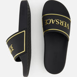 These black and gold Rubber + Embossing Versace Slide Sandals by VERSACE feature gold trim and the brand's signature logo across the straps, shown from the side and top on a white background.