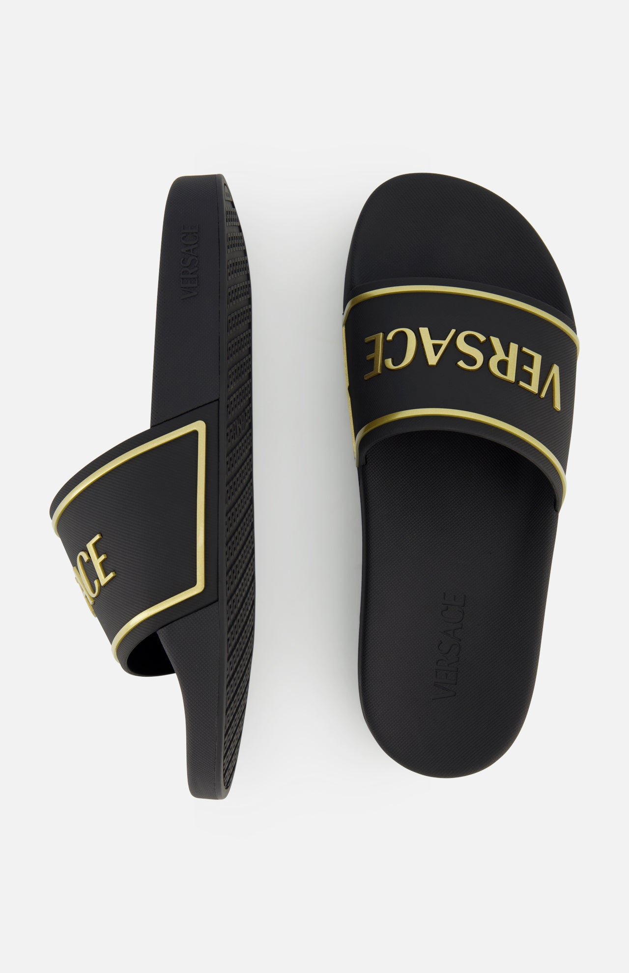 These black and gold Rubber + Embossing Versace Slide Sandals by VERSACE feature gold trim and the brand's signature logo across the straps, shown from the side and top on a white background.