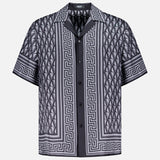 The VERSACE V Greca Print Silk Shirt is a slim-fit men’s short-sleeve shirt in black and gray with Greek key and diamond patterns, shown on a plain white background.