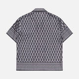The VERSACE V Greca Print Silk Shirt is a short-sleeved, slim-fit men's shirt with a black and gray geometric diamond pattern and Greek key accents on the collar, sleeves, and hem, shown against a white background.
