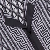 Close-up of the VERSACE V Greca Print Silk Shirt, a slim-fit men's shirt featuring a bold black, white, and gray geometric pattern with interlocking lines, black buttons, and a visible collar.