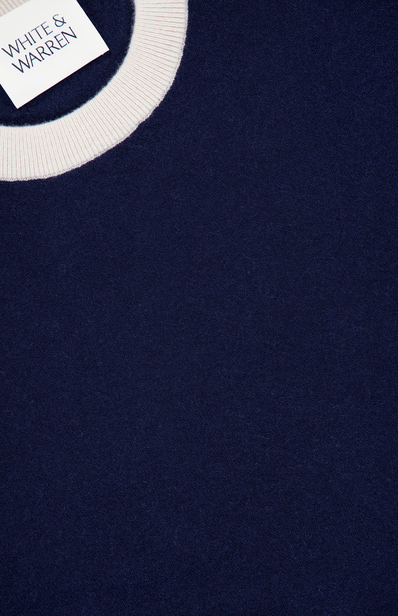 Close-up of a navy sweater featuring a white ribbed crewneck collar. A tag in the corner reads WHITE + WARREN, emphasizing the premium quality of this Cashmere Blend Relaxed Crewneck Sweater.