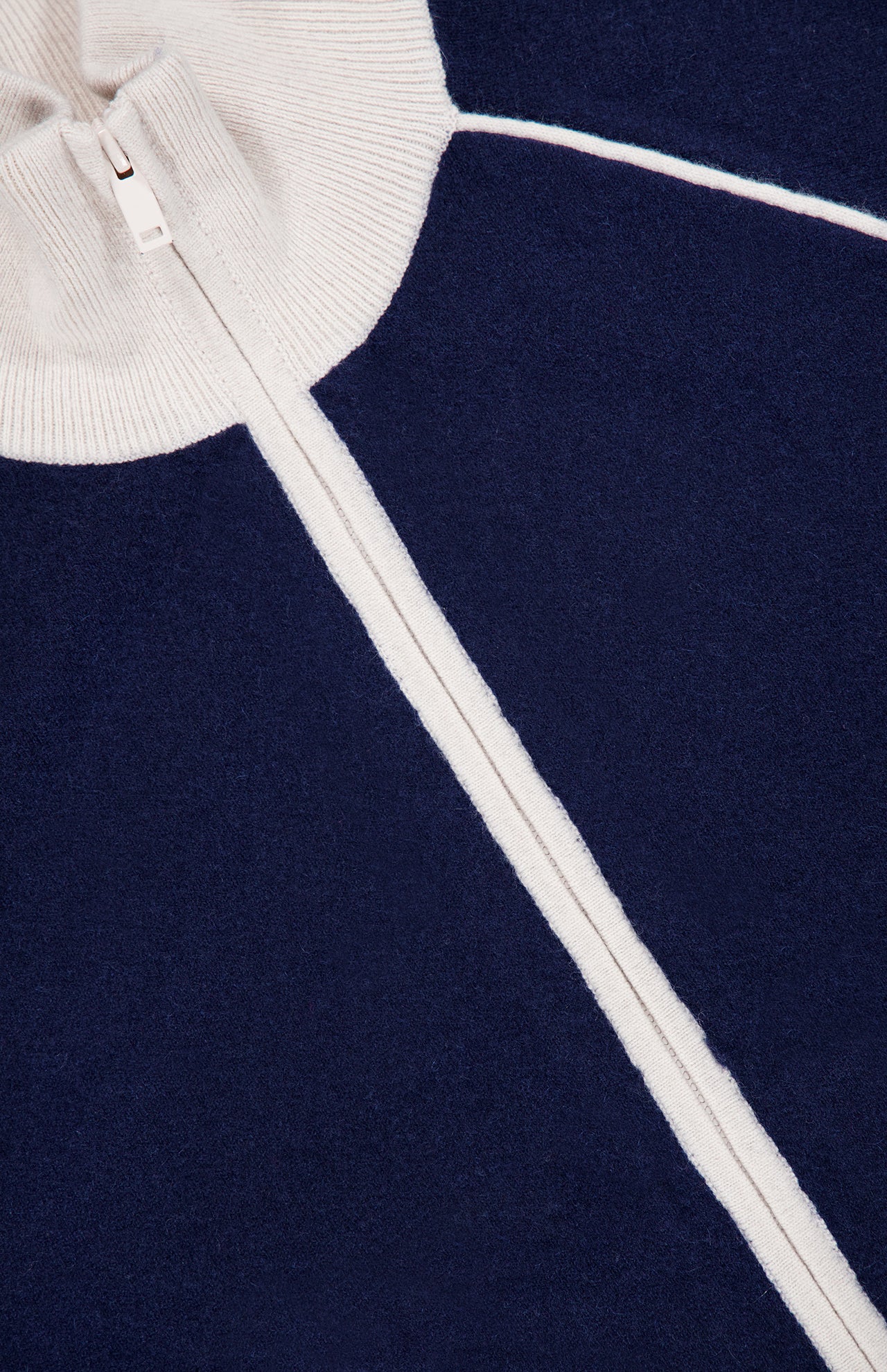 Close-up of the WHITE + WARREN Cashmere Blend Track Jacket in navy, featuring striking white accents and a visible vertical zipper. The ribbed white collar at the top and contrasting white lines on the rich knit fabric highlight the sporty, elevated design of this premium track jacket.