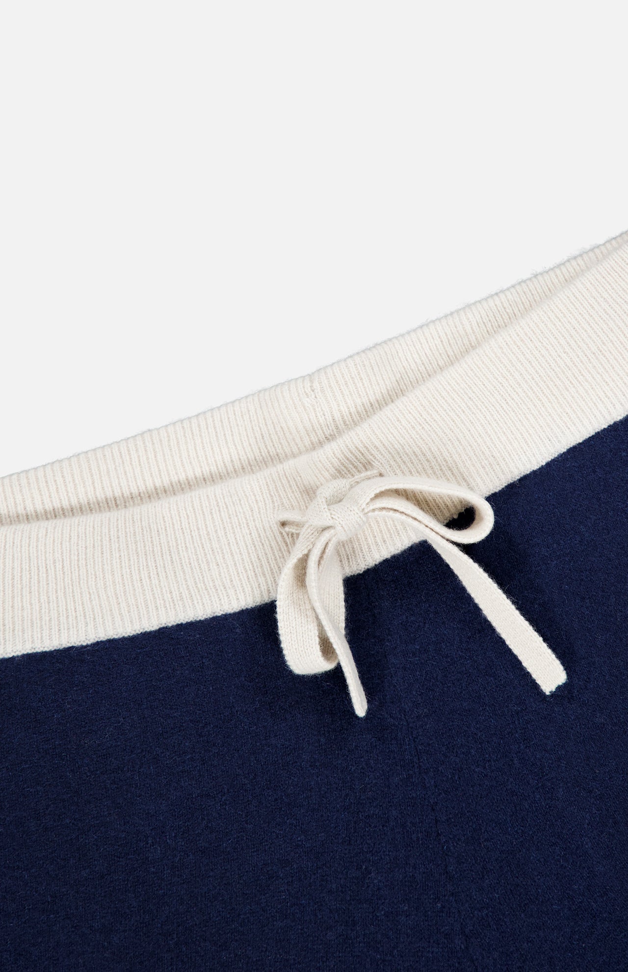 Close-up of the drawstring waist on the WHITE + WARREN Cashmere Blend Track Pants, featuring a cream-colored ribbed fabric and matching drawstring tied in a bow, set against navy fabric.
