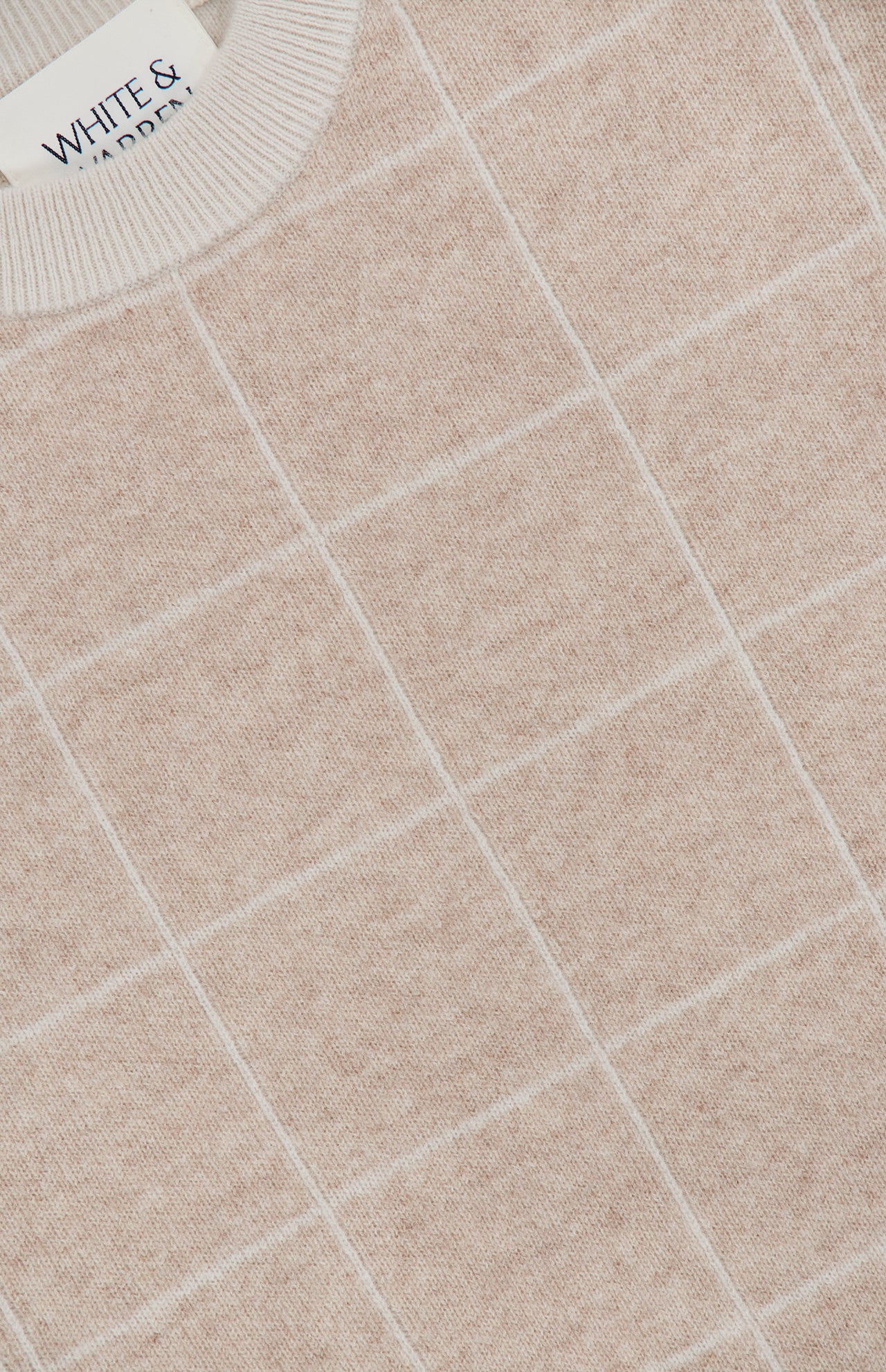 Close-up of the Cashmere Blend Windowpane Sweater by WHITE + WARREN in beige, featuring a subtle white grid pattern. A portion of the WHITE + WARREN label is visible at the collar. The cozy knit top looks soft and textured.