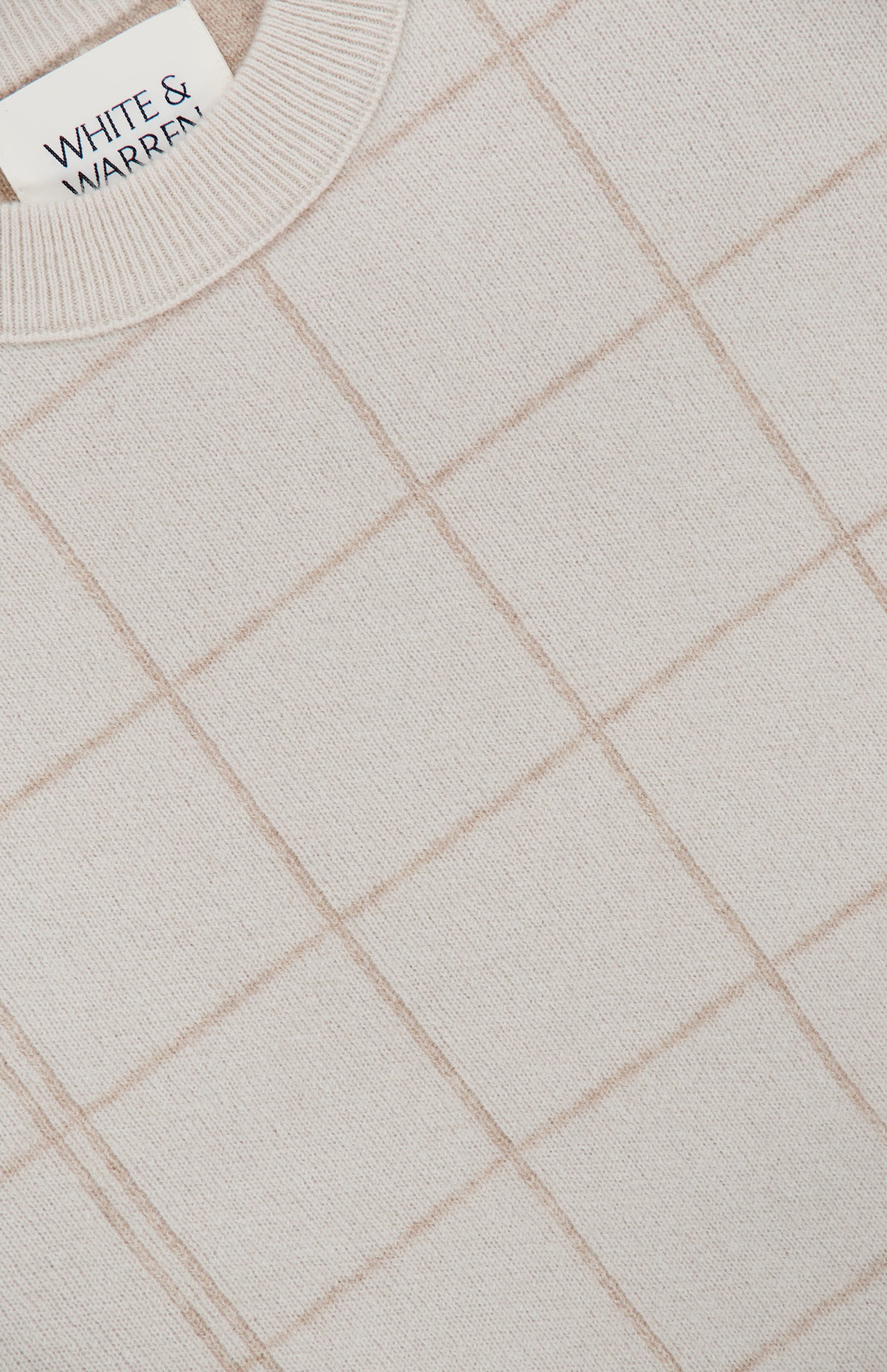 A close-up of the Cashmere Blend Windowpane Sweater by WHITE + WARREN, featuring a beige knit with a light brown windowpane grid pattern crafted from a luxurious wool-cashmere blend. The cozy sweater displays the signature WHITE + WARREN label near the collar.