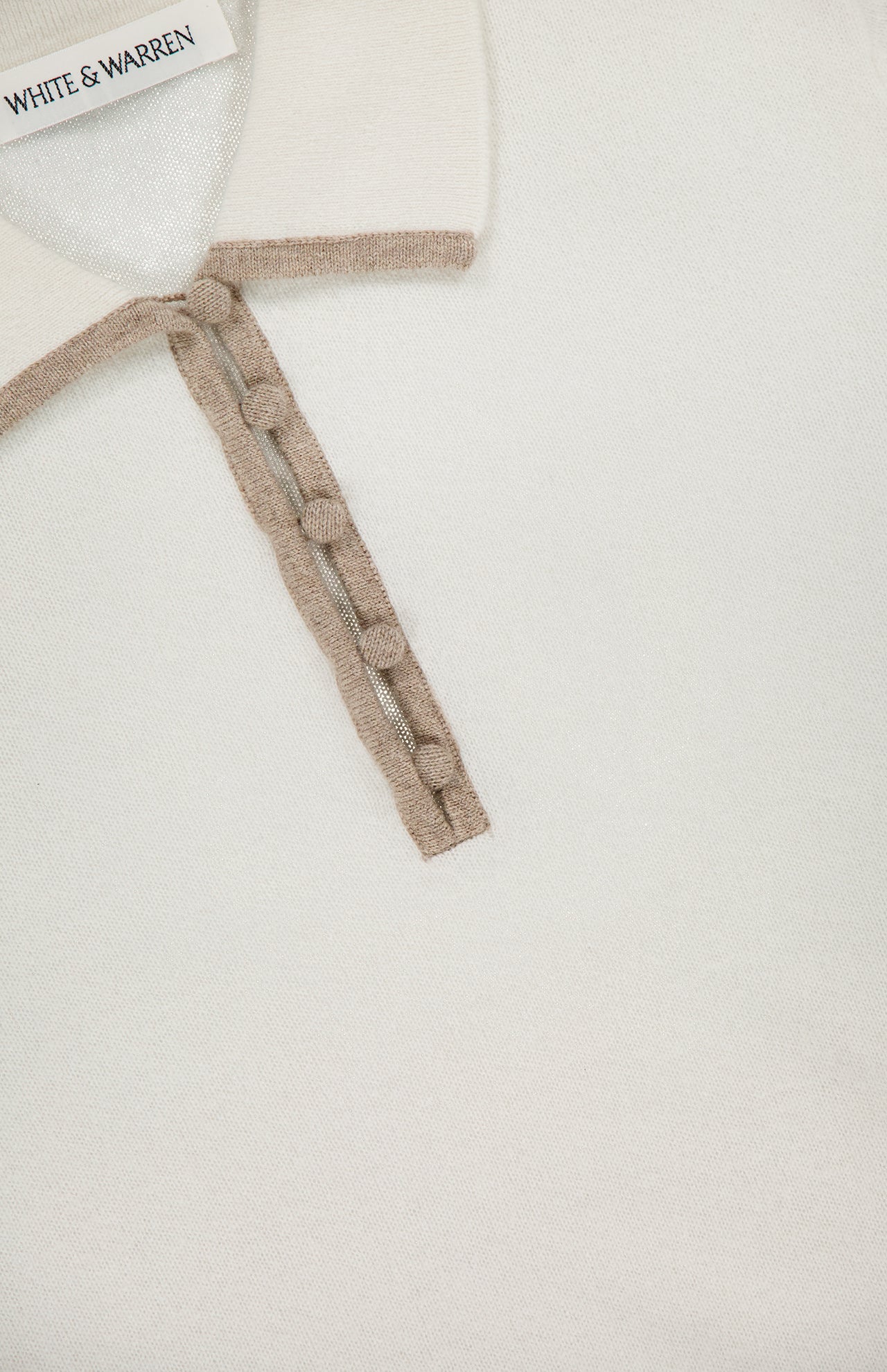 Close-up of the Cashmere Button Polo Shirt by WHITE + WARREN, an off-white collared sweater with beige trim and button placket; the brand label appears inside the collar.