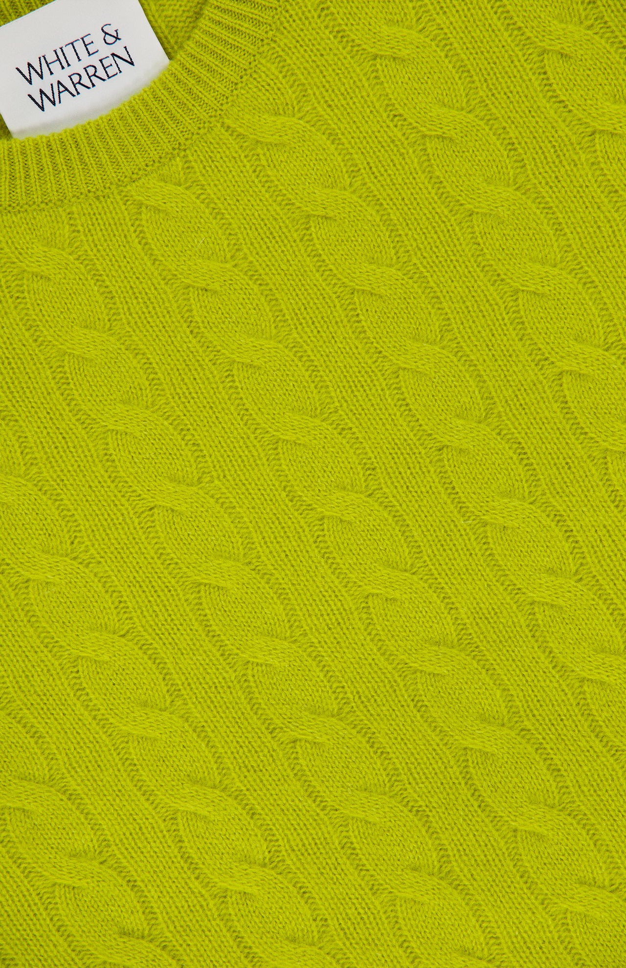 Close-up of a bright green Cashmere Cable Crewneck Sweater featuring a cableknit design and ribbed neckline. A white label in the top left corner displays WHITE + WARREN.
