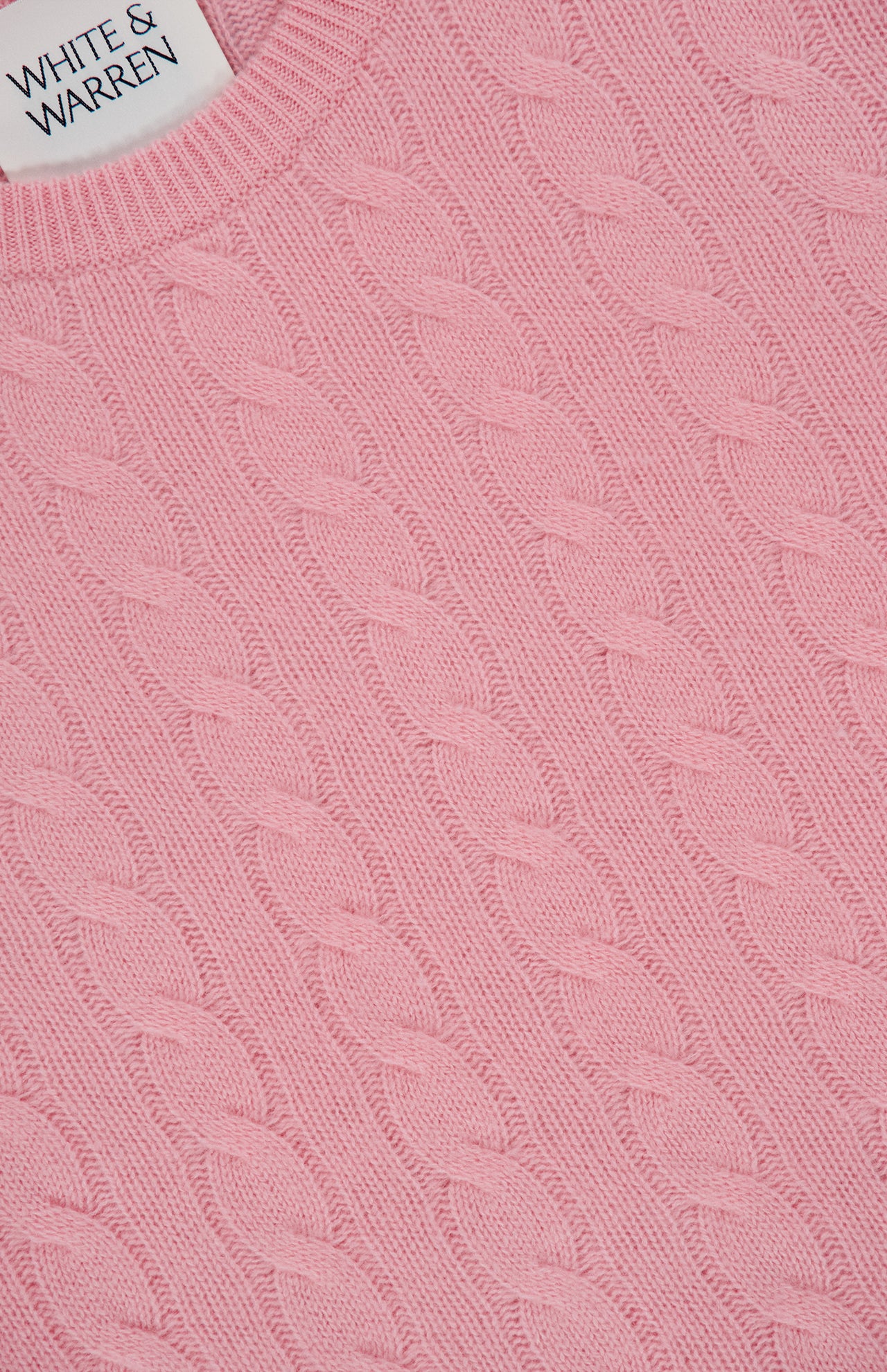 Close-up of a pink Cashmere Cable Crewneck Sweater with a visible WHITE + WARREN label in the top left corner, highlighting the soft texture of this luxurious cashmere piece.