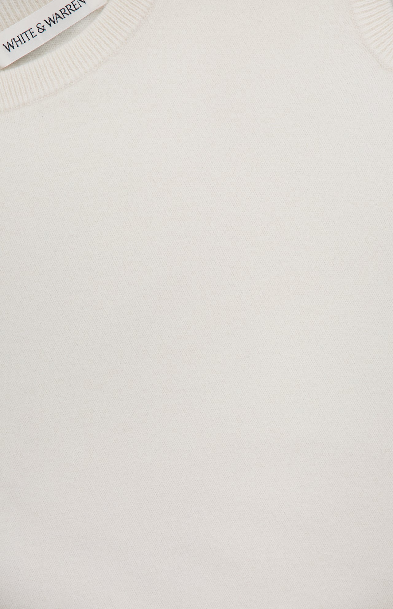 Close-up of WHITE + WARREN's Cashmere Off Shoulder Top in a cream shade with a ribbed neckline; the brand label appears in the top left corner.
