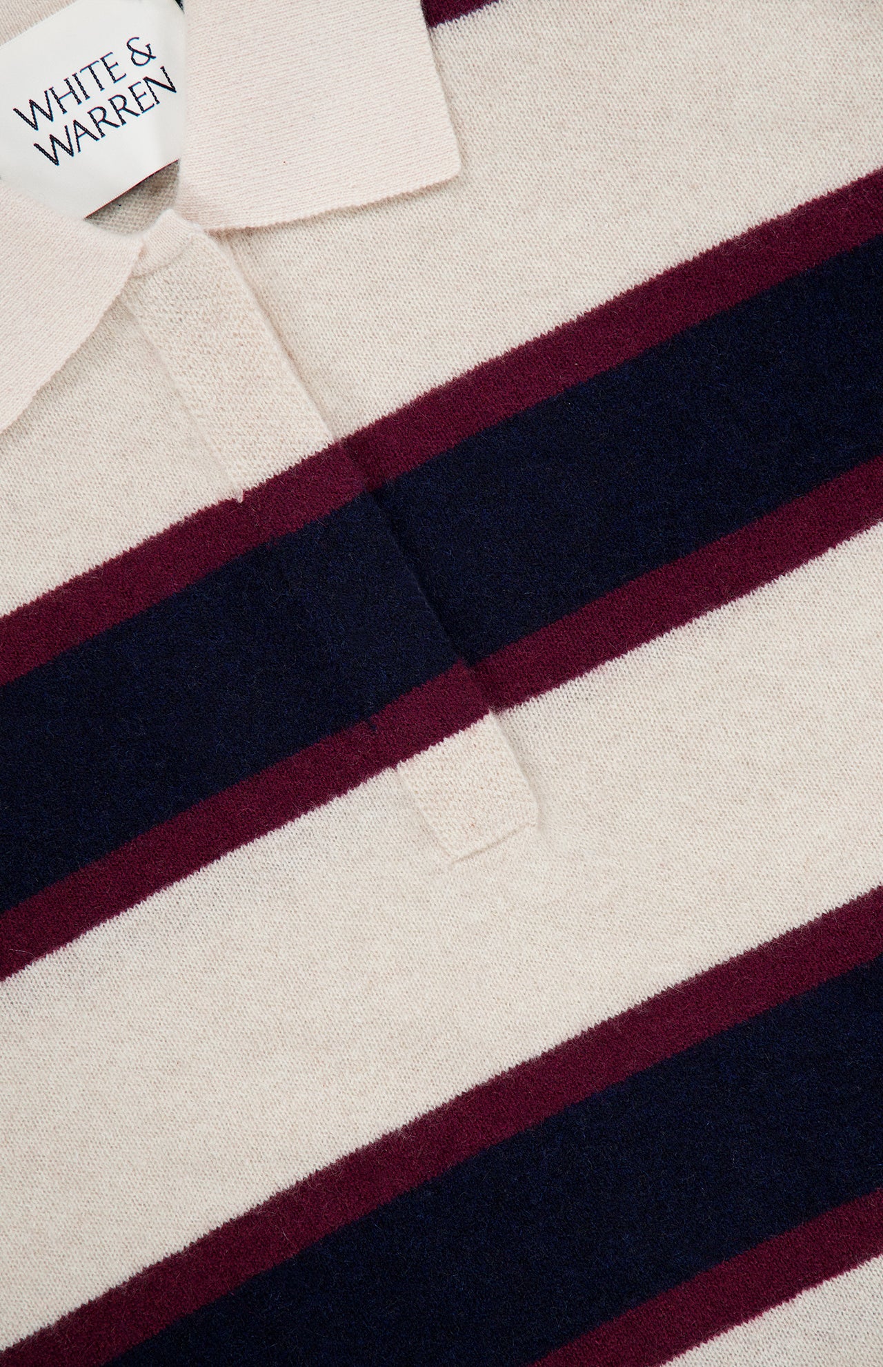 Close-up of the Cashmere Rugby Long Sleeve Polo Shirt by WHITE + WARREN, featuring cream, navy blue, and burgundy horizontal stripes inspired by the rugby trend. The shirt is finished with a cream collar and a WHITE + WARREN label.