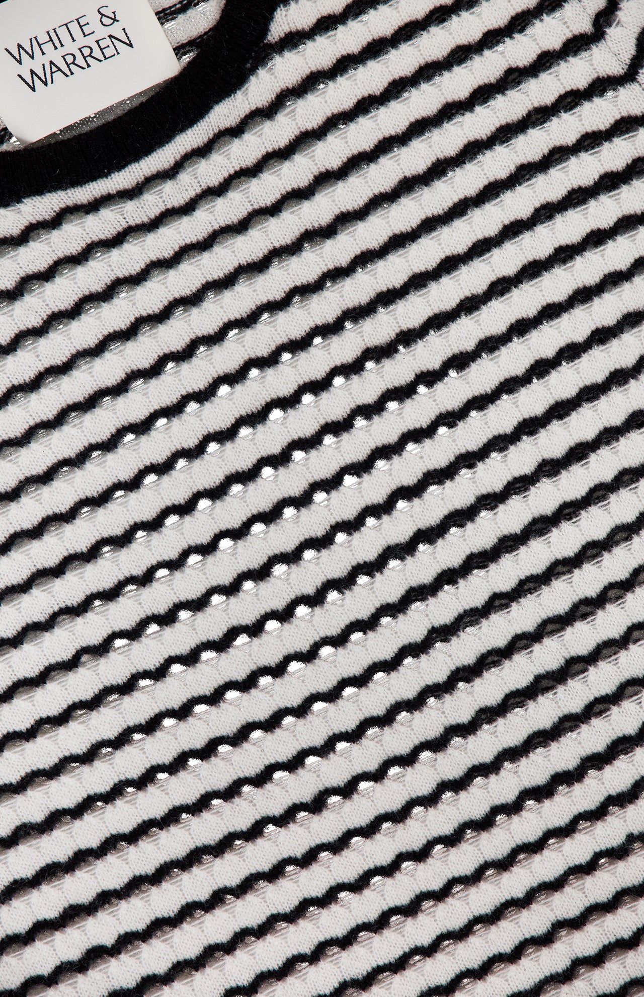 Close-up of the WHITE + WARREN Cashmere Striped Long Sleeve Top in black and white with bold stripes, a textured, slightly open weave, and the brand label visible in the top left corner.