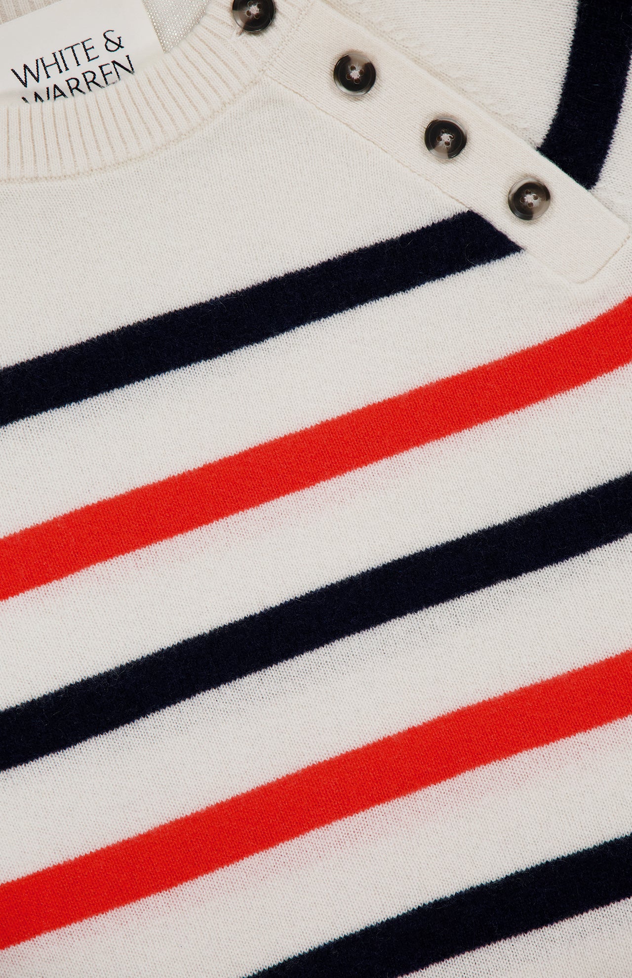 Close-up of the WHITE + WARREN Cashmere Striped Sweater, featuring off-white fabric with red and navy blue stripes, silver shoulder buttons, and a visible brand label on the collar.