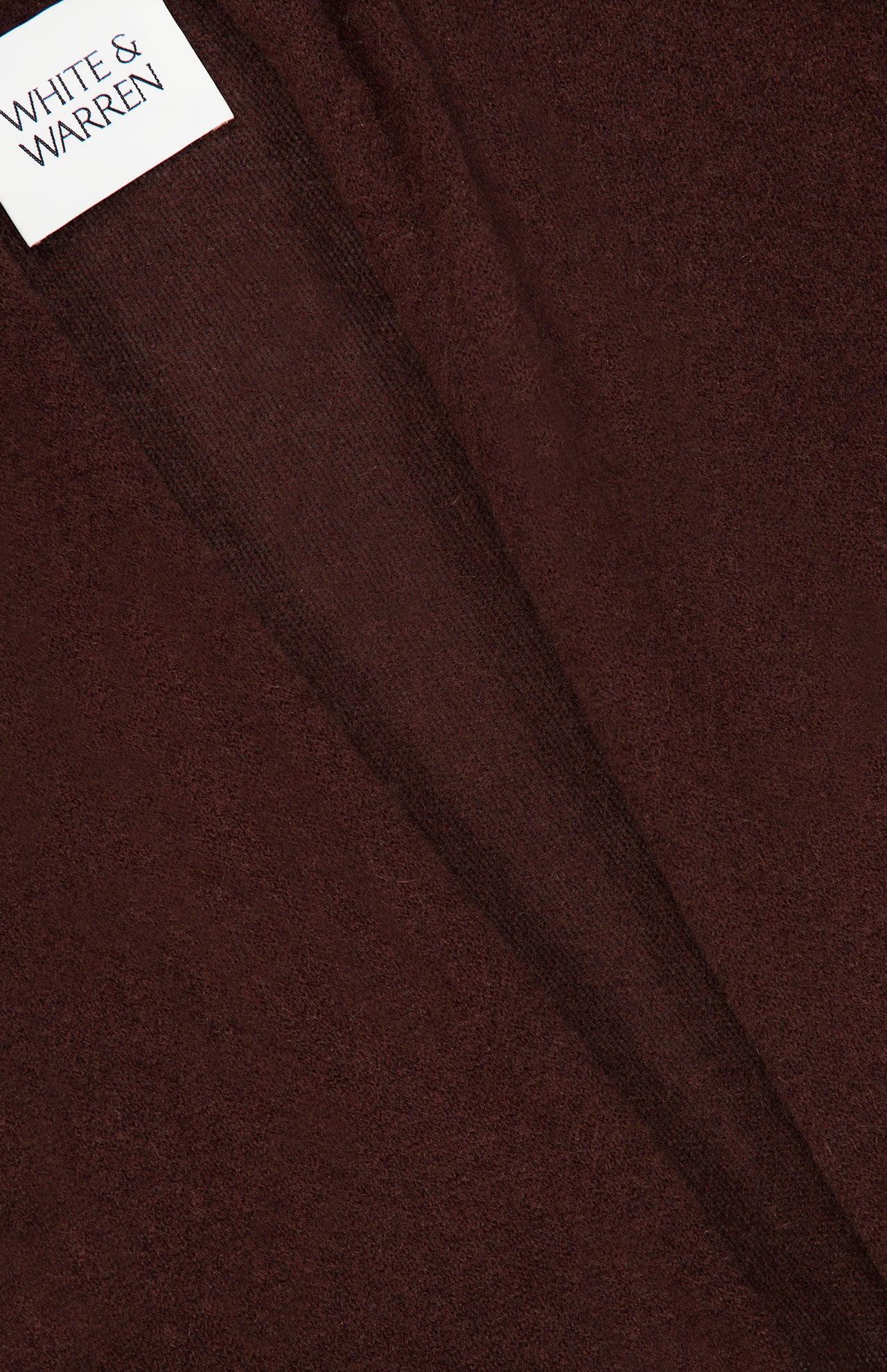Close-up of the dark brown Cashmere Trapeze Cardigan fabric with a visible seam and a white label reading WHITE + WARREN in black text sewn into the top left corner.