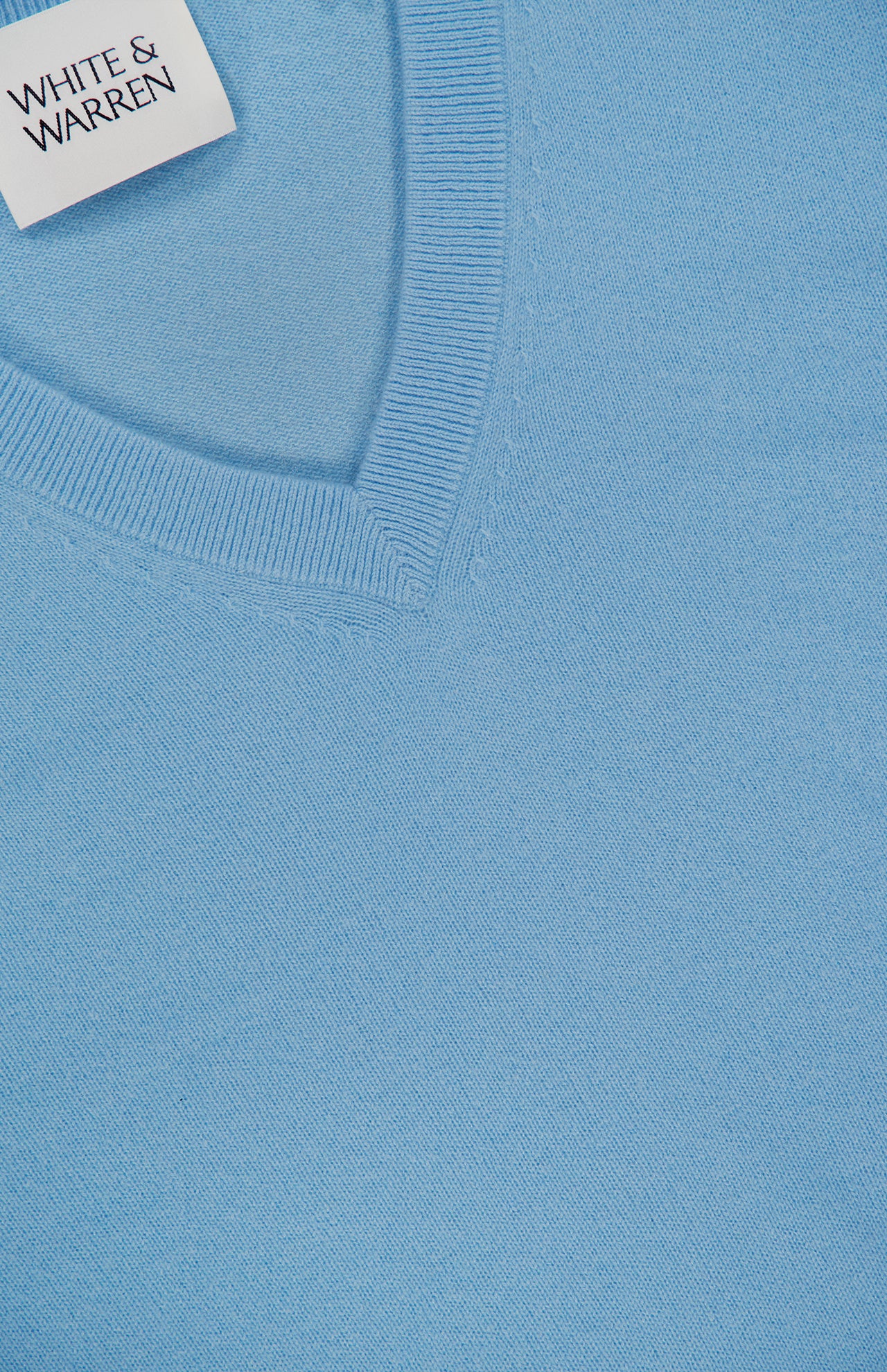 Close-up of a light blue Cashmere V-neck Sweater featuring visible ribbed edging and a WHITE + WARREN label sewn into the neckline.