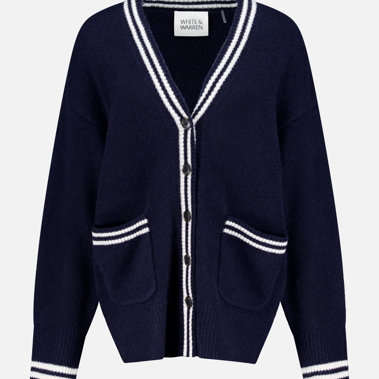 The WHITE + WARREN Cashmere Varsity Cardigan is a navy boyfriend-style piece with white stripes on the collar, cuffs, hem, and pockets. It features a V-neck, front buttons, two front pockets, and “White + Warren” labeling.