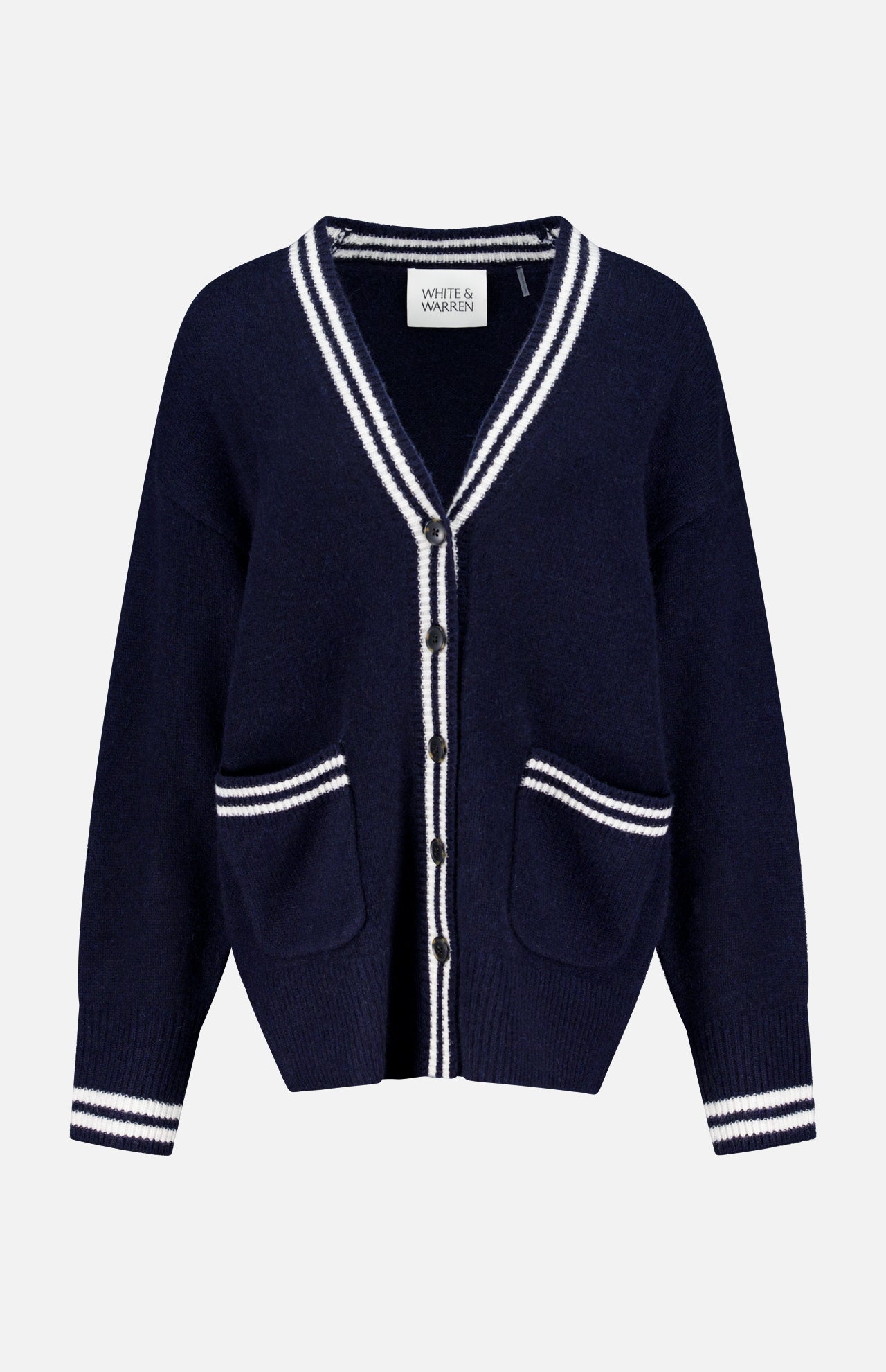 The WHITE + WARREN Cashmere Varsity Cardigan is a navy boyfriend-style piece with white stripes on the collar, cuffs, hem, and pockets. It features a V-neck, front buttons, two front pockets, and “White + Warren” labeling.
