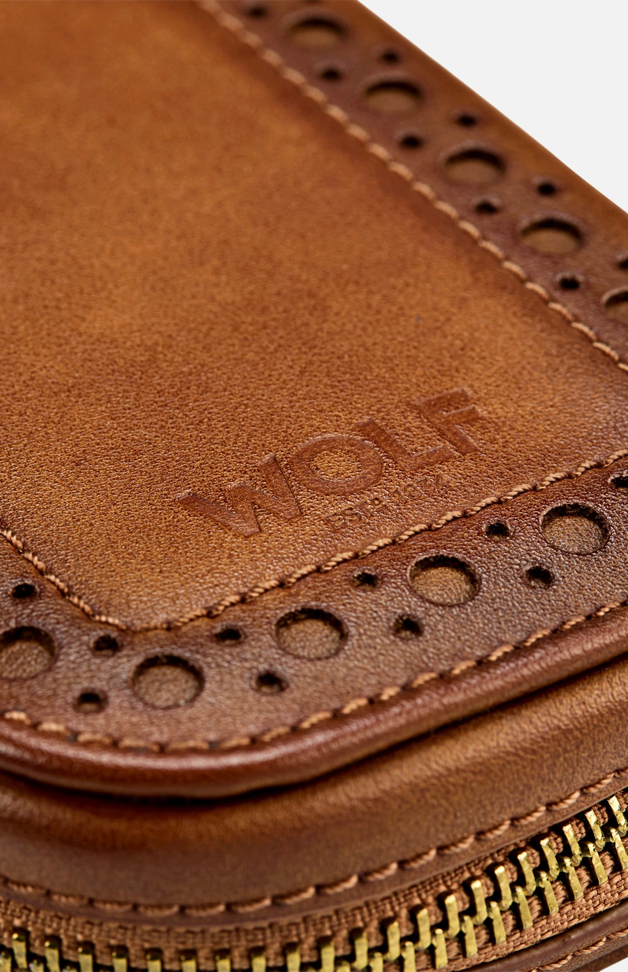 Close-up of the WOLF Brogue 2 Piece Watch Zip Case in brown leather, featuring decorative perforations, detailed stitching, and a gold zipper. The word "WOLF" is embossed on the leather surface, highlighting luxury storage for watches in this elegant case.