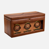 The WOLF Brogue Triple Winder with Storage is a brown leather luxury watch winder box featuring three circular slots, each labeled with the WOLF logo, decorative stitching, and a transparent front panel for elegant triple watch storage.