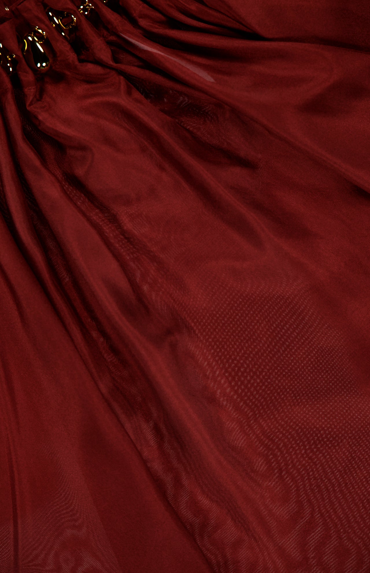 The ZIMMERMANN Aster Gathered Bead Blouse features deep burgundy sheer fabric gathered with gold rings, creating soft pleats and a subtle shine for an elegant, merlot-inspired look.