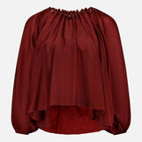 The ZIMMERMANN Aster Gathered Bead Blouse is a loose-fitting, long-sleeve bohemian top in dark red, featuring a grommet-detailed neckline and flowy asymmetrical hem, shown against a plain white background.