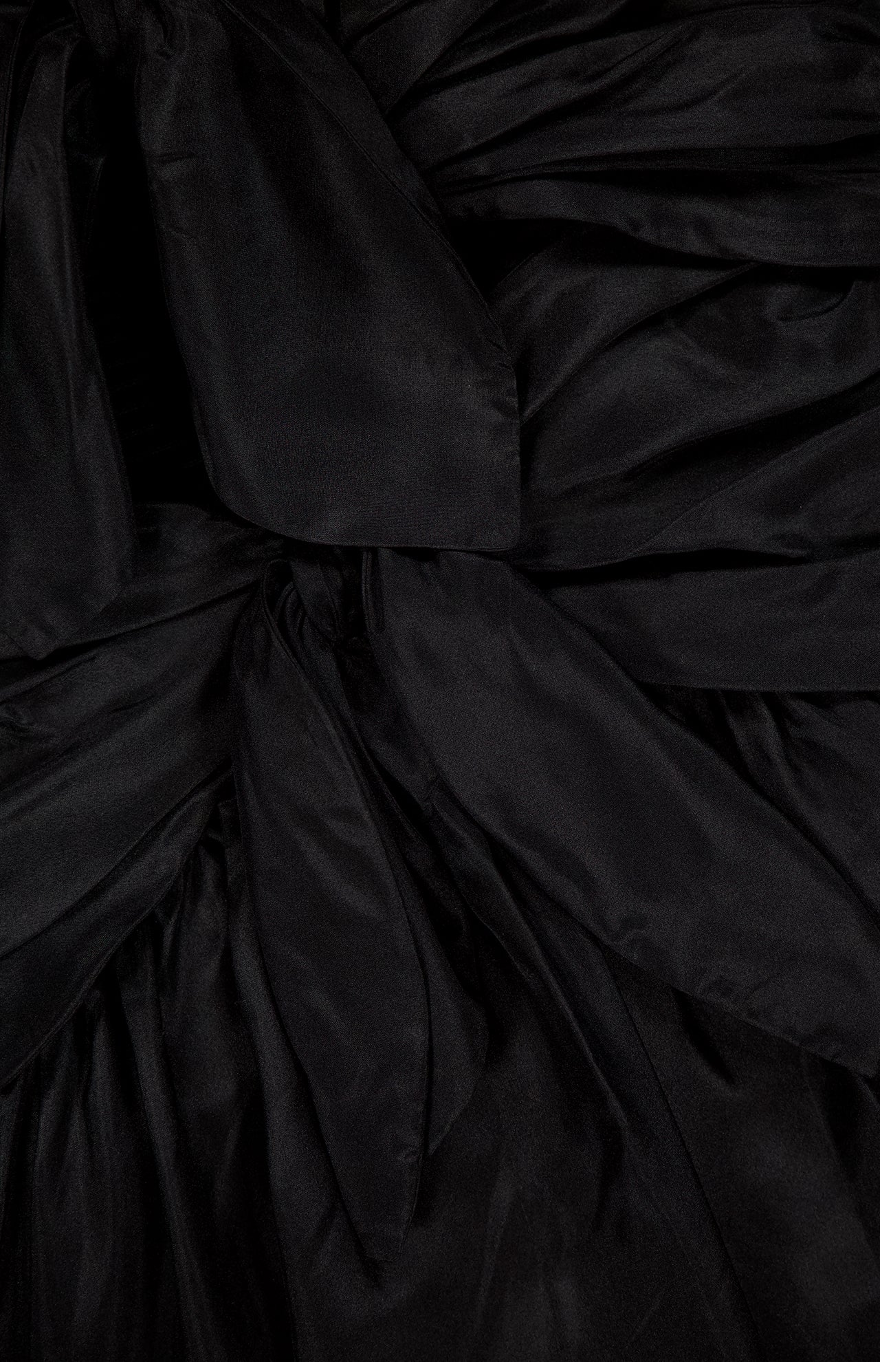 Close-up of the black, shiny, pleated fabric from ZIMMERMANN'S Aster Scarf Silk Midi Dress, featuring overlapping layers and folds for a textured and slightly glossy look.