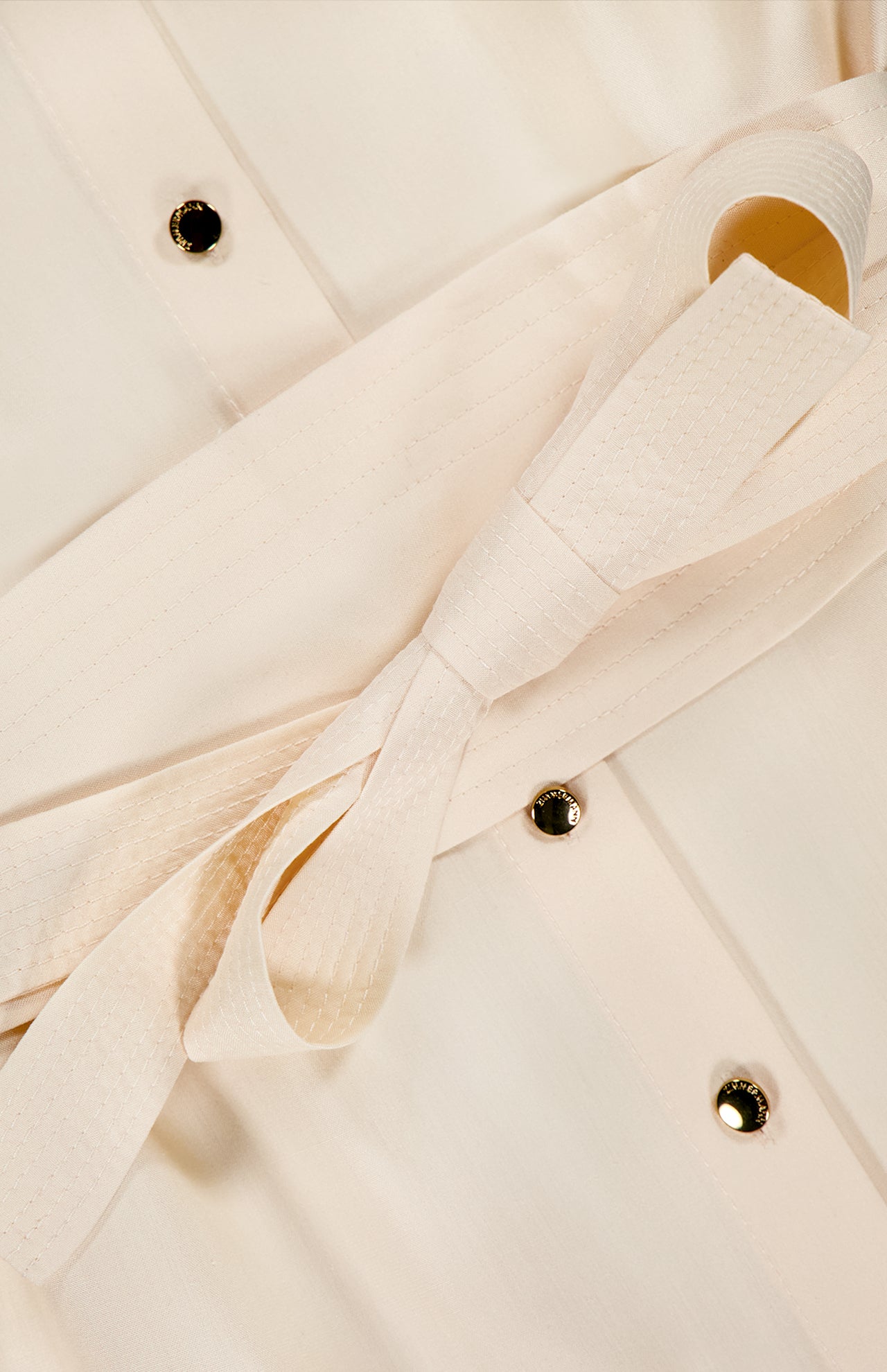 Close-up of the Luna Obi Silk Midi Dress by ZIMMERMANN, featuring a fabric belt tied in a bow and round gold buttons on the front. The subtly textured silk fabric enhances the elegant, feminine design.