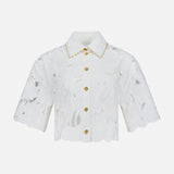 The ZIMMERMANN Mahon Embroidered Crop Shirt is an ivory short-sleeve button-up blouse with a floral cut-out pattern, gold buttons, scalloped edges, and embroidered cotton detail along the collar.