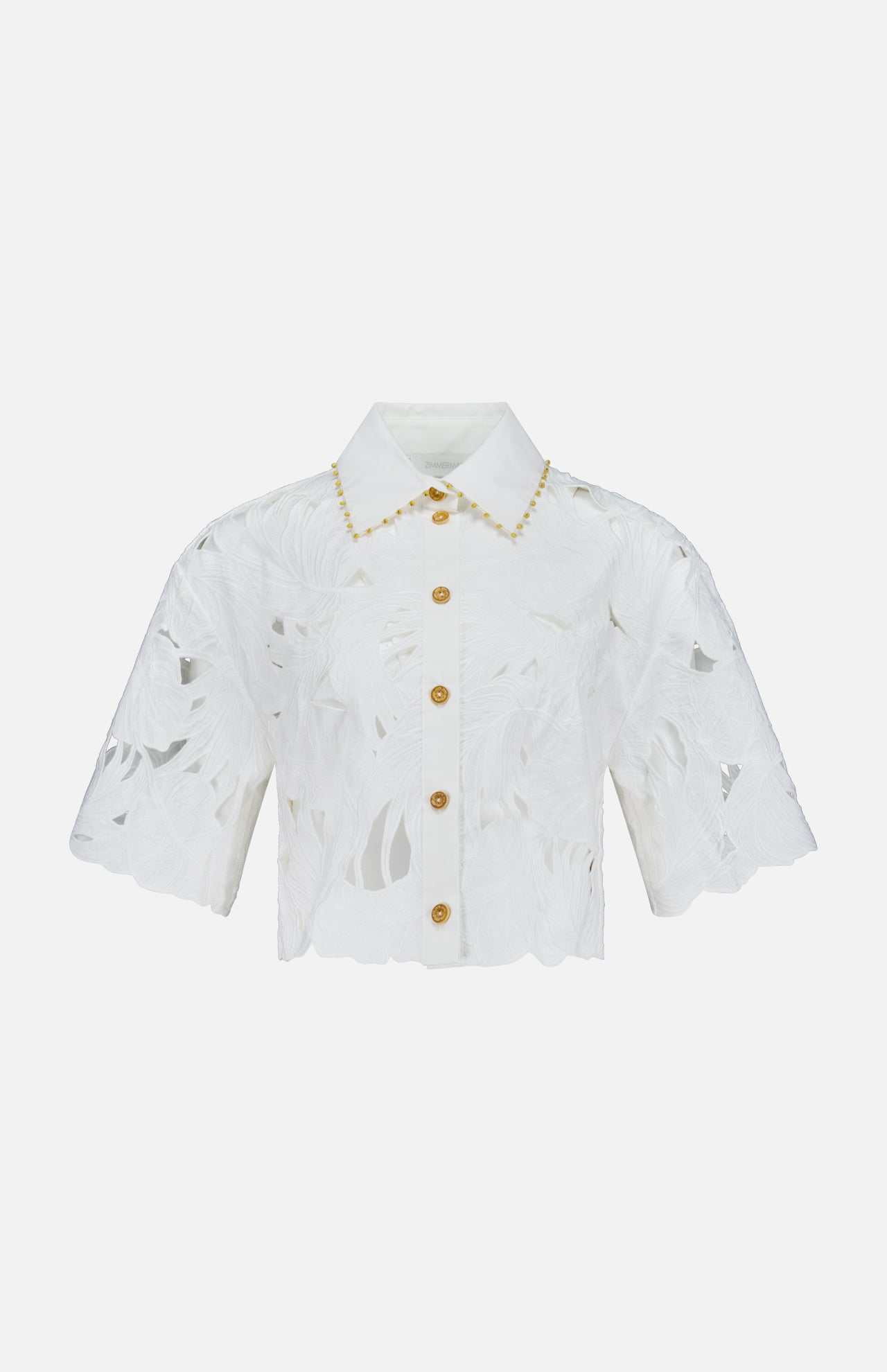 The ZIMMERMANN Mahon Embroidered Crop Shirt is an ivory short-sleeve button-up blouse with a floral cut-out pattern, gold buttons, scalloped edges, and embroidered cotton detail along the collar.