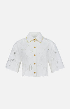 The ZIMMERMANN Mahon Embroidered Crop Shirt is an ivory short-sleeve button-up blouse with a floral cut-out pattern, gold buttons, scalloped edges, and embroidered cotton detail along the collar.