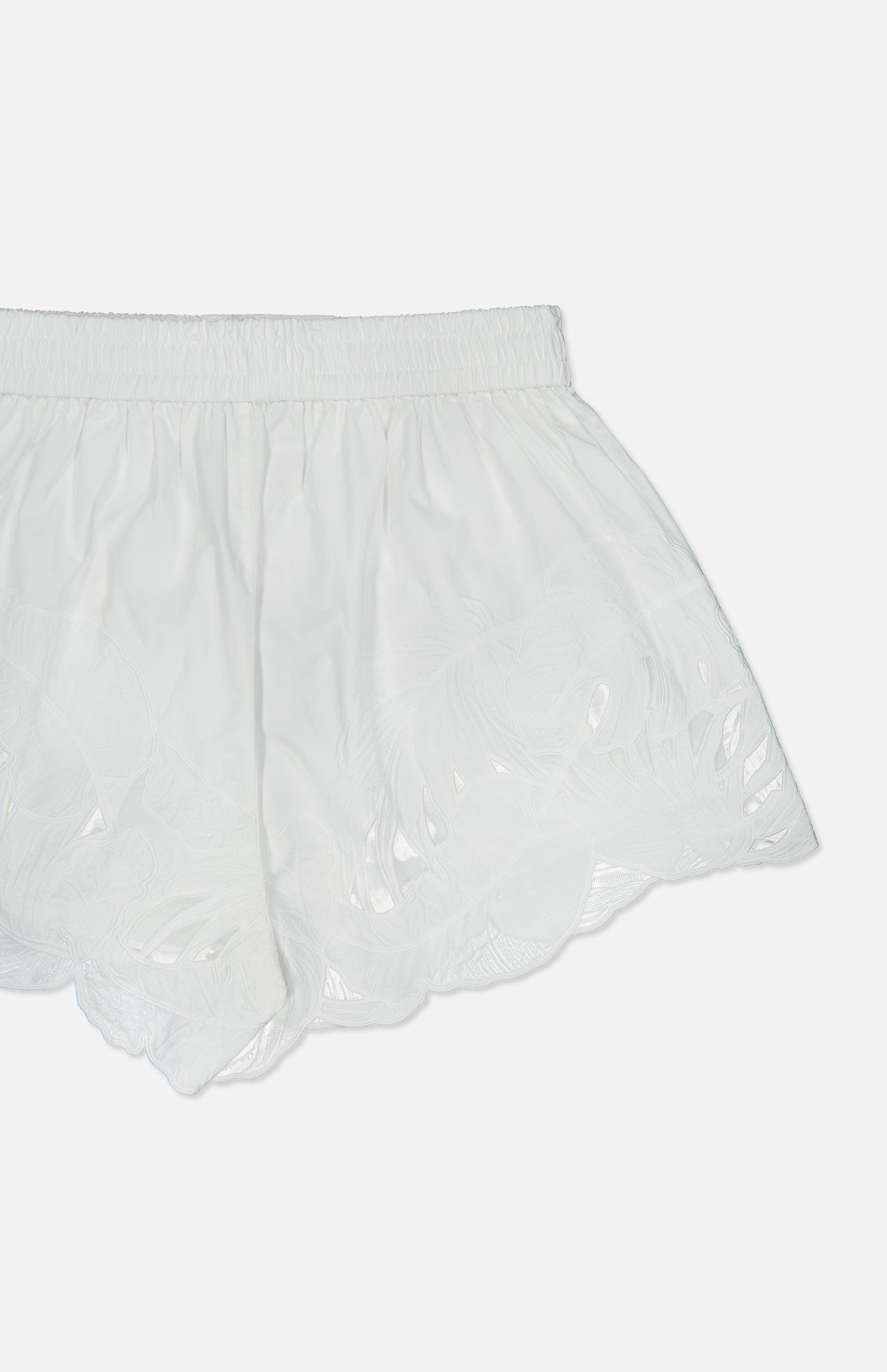 The Mahon Embroidered Drawstring Short by ZIMMERMANN features white, semi-sheer high-rise shorts with an elastic waistband and delicate embroidery along the scalloped hem, shown on a plain white background.